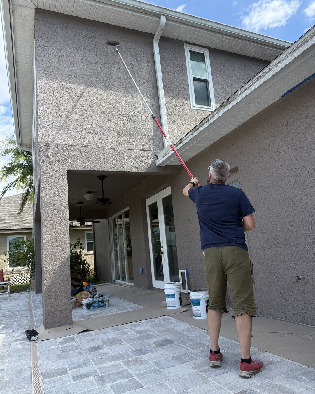 Our painter rolling the upper wall of a two-story stucco home in Westchase, Tampa